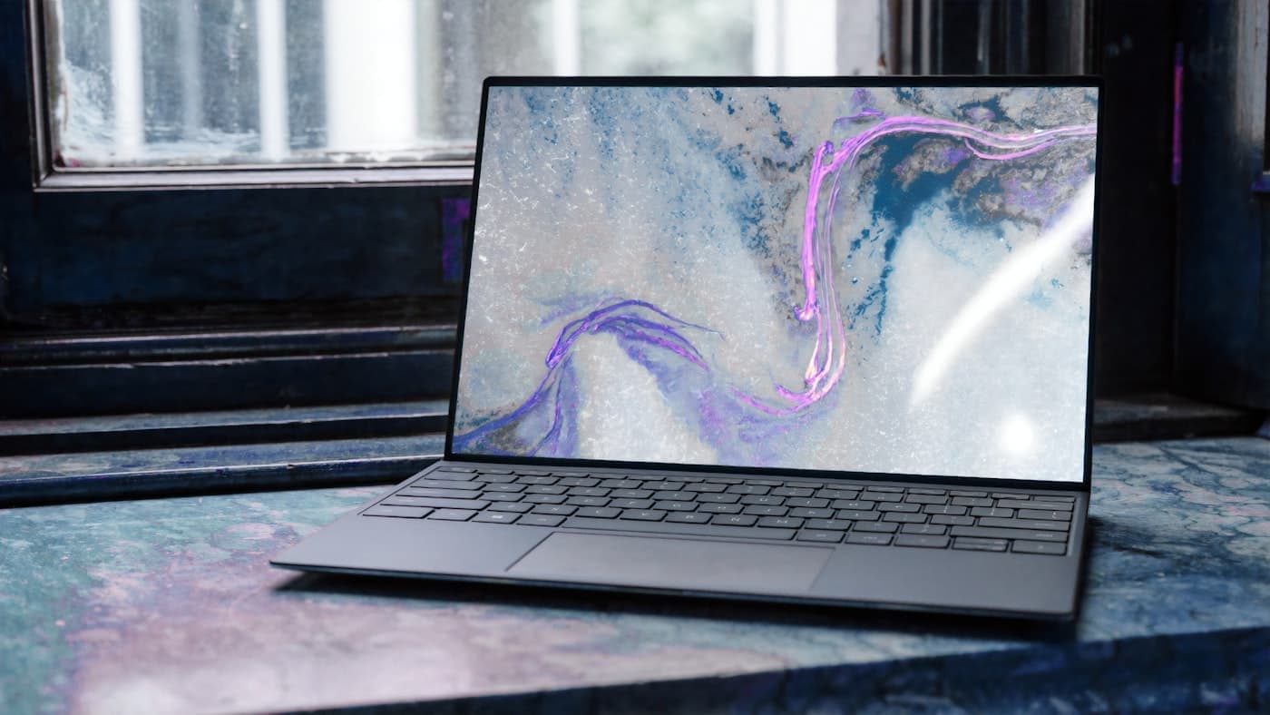 Dell XPS laptop open on a white desk, screen showing a swirl wallpaper