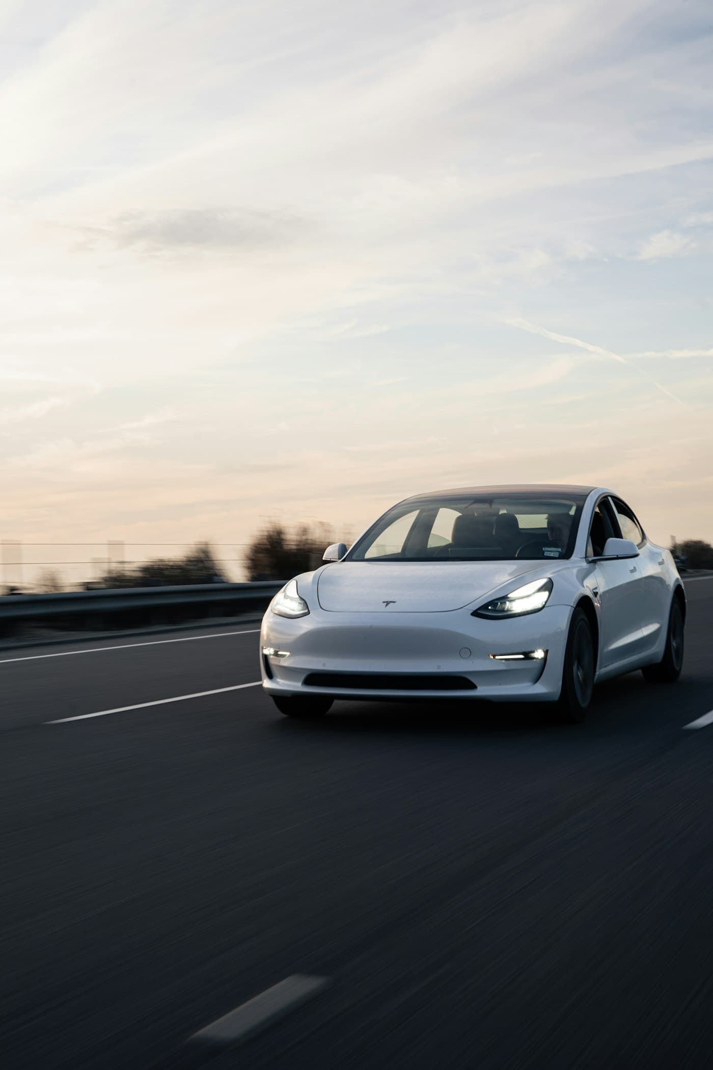 White Tesla Model 3 driving on a road at dusk